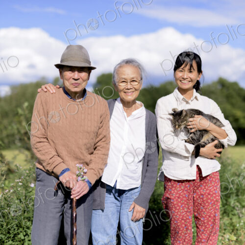 Smiling woman holding grey cat standing outdoors, with an elderly man and woman,…