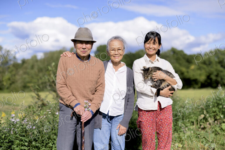 Smiling woman holding grey cat standing outdoors, with an elderly man and woman,…