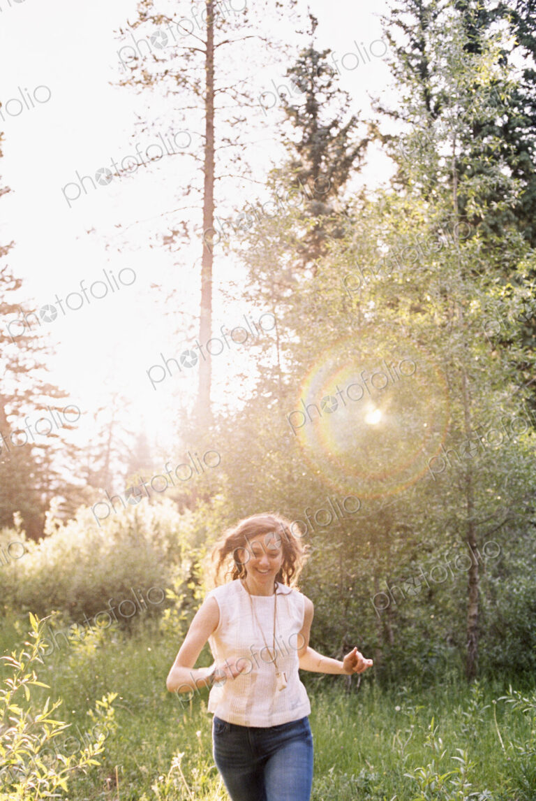 Smiling woman running through a sunlit forest.