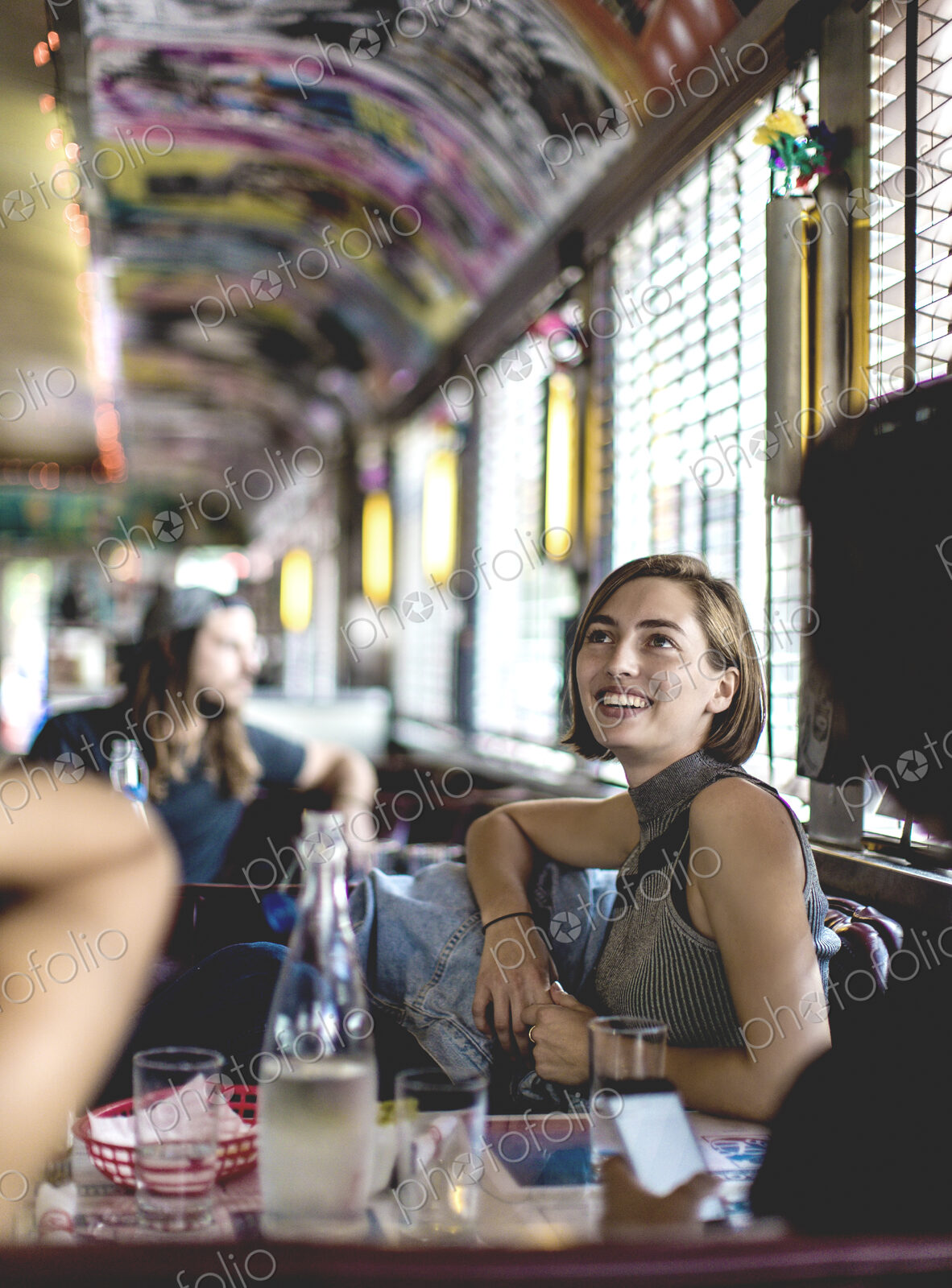 Smiling woman sitting in a booth in a diner looking up and talking to friends.