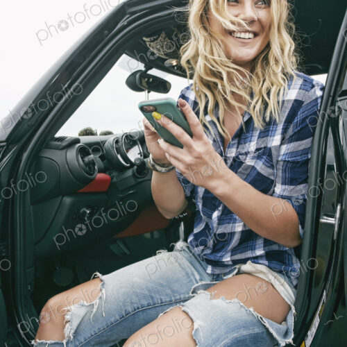 Smiling woman sitting in car, holding mobile phone.