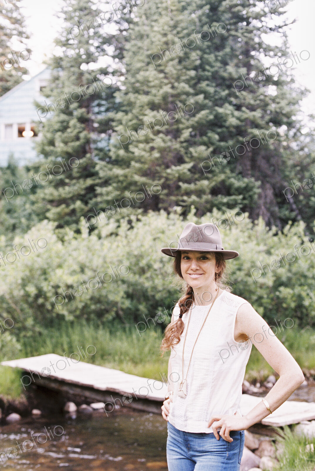 Smiling woman standing by a wooden bridge over a stream.
