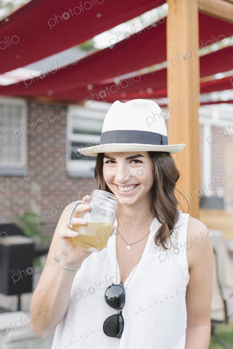 Smiling woman standing in a garden, holding a drink.