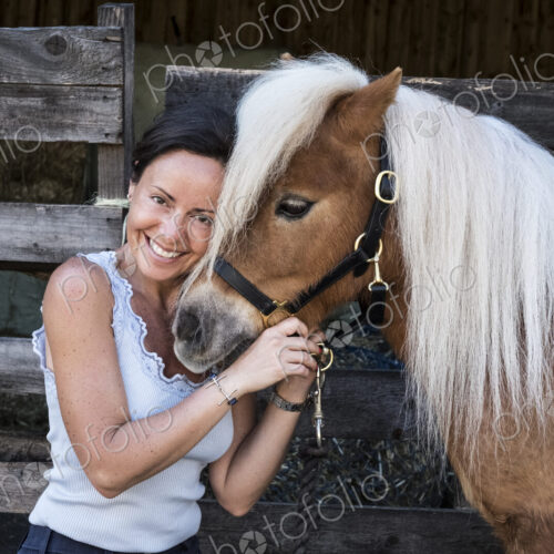 Smiling woman standing outside stable, holding a Shetland pony Smiling woman standing outside stable, holding a Shetland pony