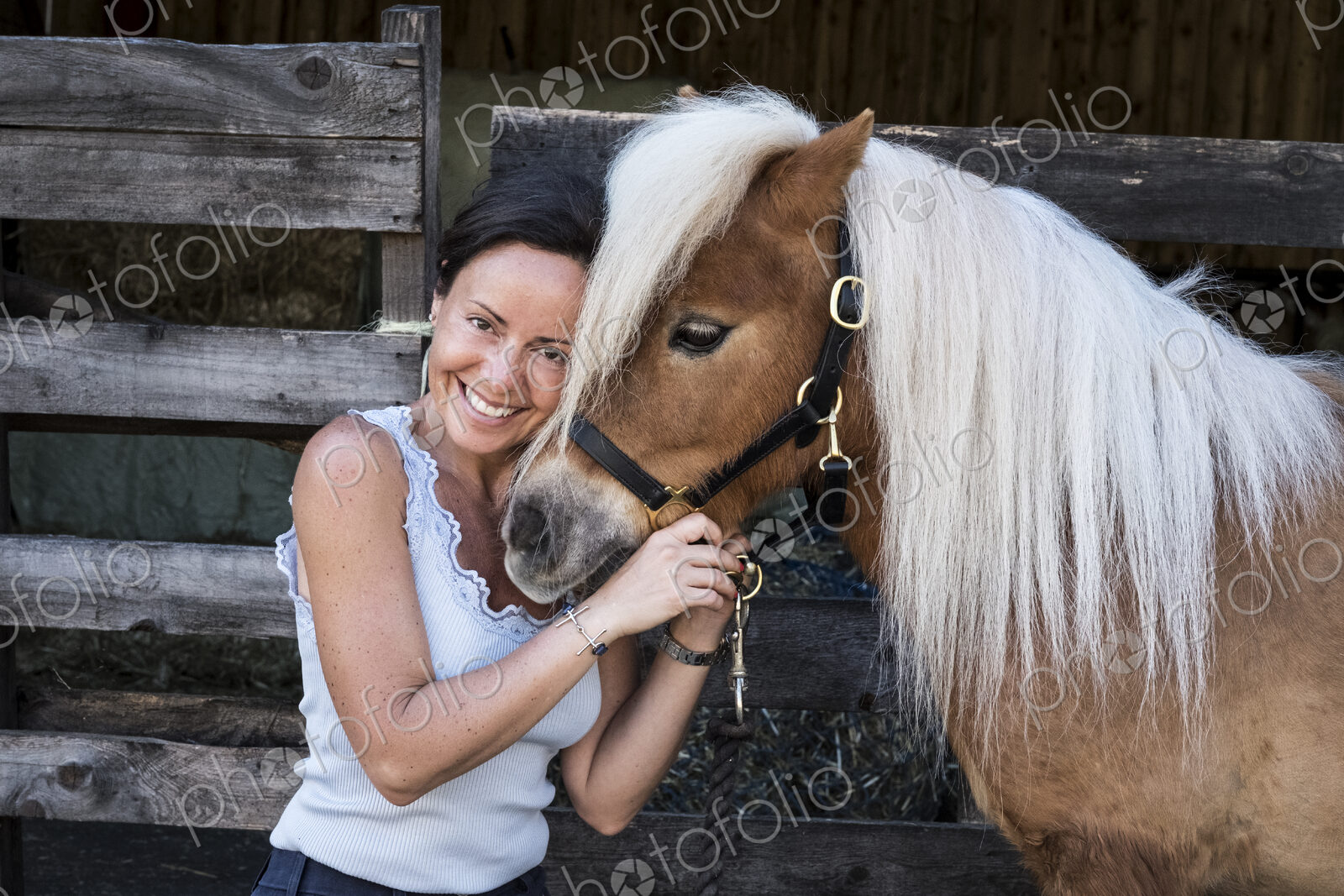 Smiling woman standing outside stable, holding a Shetland pony