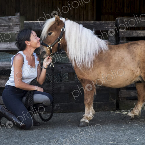 Smiling woman standing outside stable, holding a Shetland pony by its rein. Smiling woman standing outside stable, holding a Shetland pony by its rein.