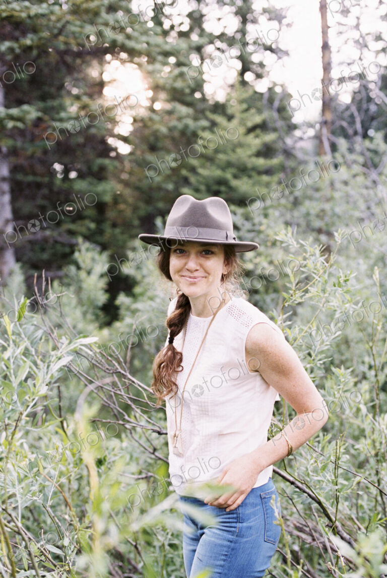 Smiling woman wearing a hat standing in a forest.