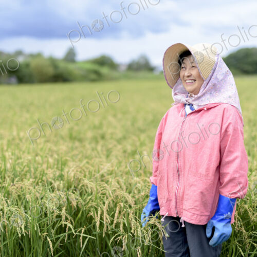 Smiling woman wearing straw hat and pink jacket and blue rubber gloves standing in a…