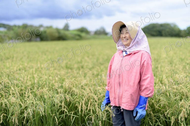 Smiling woman wearing straw hat and pink jacket and blue rubber gloves standing in a…