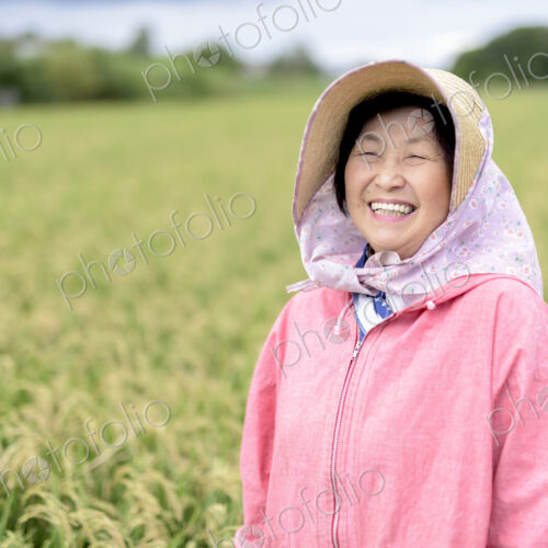 Smiling woman wearing straw hat and pink jacket standing in a rice field, looking at…