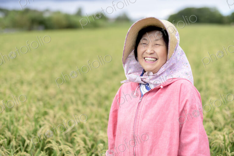 Smiling woman wearing straw hat and pink jacket standing in a rice field, looking at…