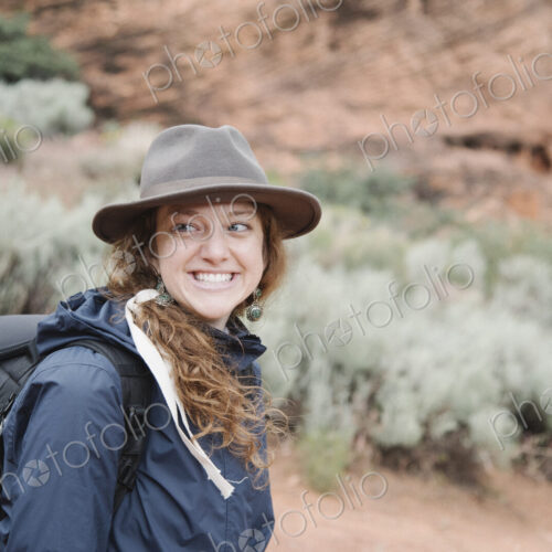 Smiling woman with auburn hair, wearing a hat and carrying a backpack, hiking in a canyon. Smiling woman with auburn hair, wearing a hat and carrying a backpack, hiking in a canyon.