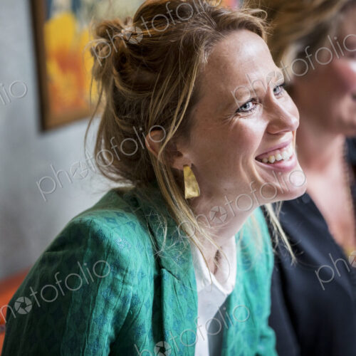 Smiling woman with blond hair wearing golden earrings and green jacket sitting at table. Smiling woman with blond hair wearing golden earrings and green jacket sitting at table.