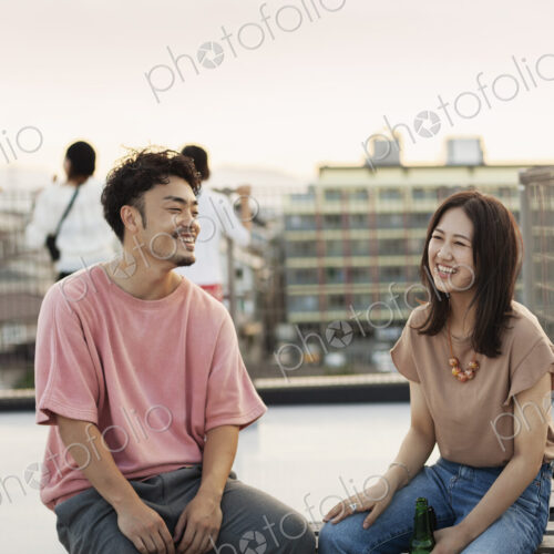 Smiling young Japanese man and woman sitting on a rooftop in an urban setting.