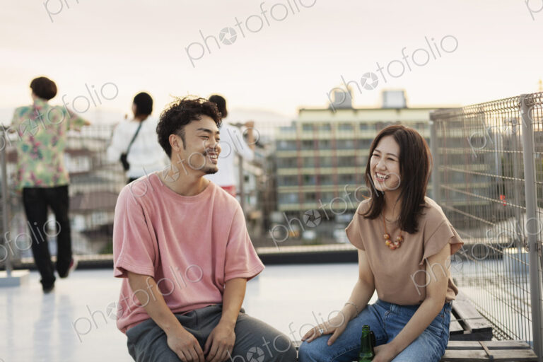 Smiling young Japanese man and woman sitting on a rooftop in an urban setting.