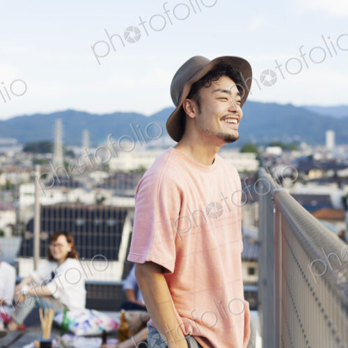 Smiling young Japanese man standing on a rooftop in an urban setting.