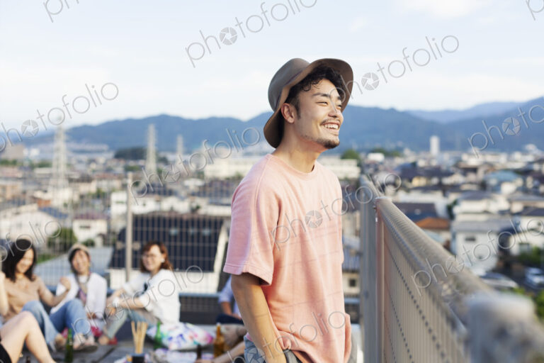 Smiling young Japanese man standing on a rooftop in an urban setting.
