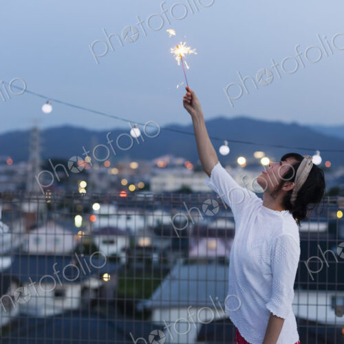 Smiling young Japanese woman holding sparkler on a rooftop in an urban setting. Smiling young Japanese woman holding sparkler on a rooftop in an urban setting.