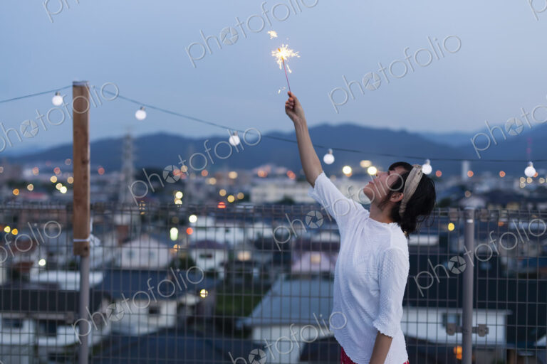 Smiling young Japanese woman holding sparkler on a rooftop in an urban setting.