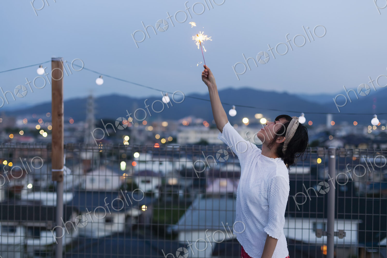 Smiling young Japanese woman holding sparkler on a rooftop in an urban setting.