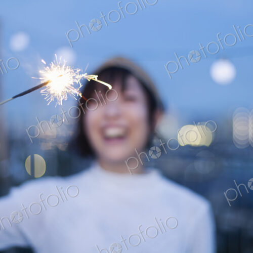 Smiling young Japanese woman holding sparkler on a rooftop in an urban setting. Smiling young Japanese woman holding sparkler on a rooftop in an urban setting.