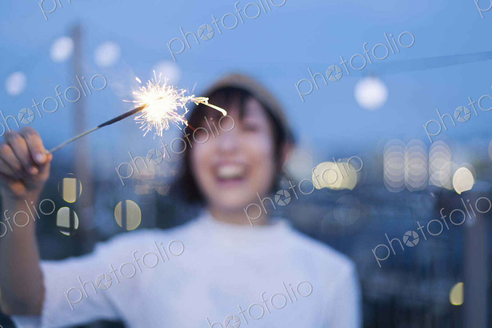 Smiling young Japanese woman holding sparkler on a rooftop in an urban setting.