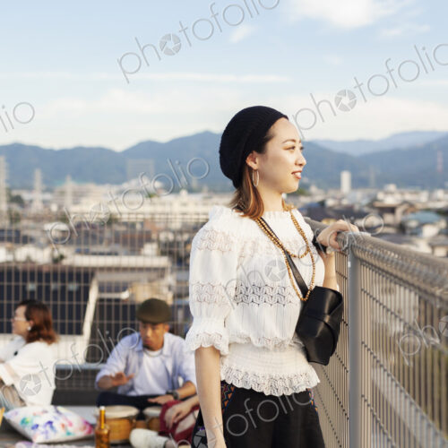 Smiling young Japanese woman standing on a rooftop in an urban setting.