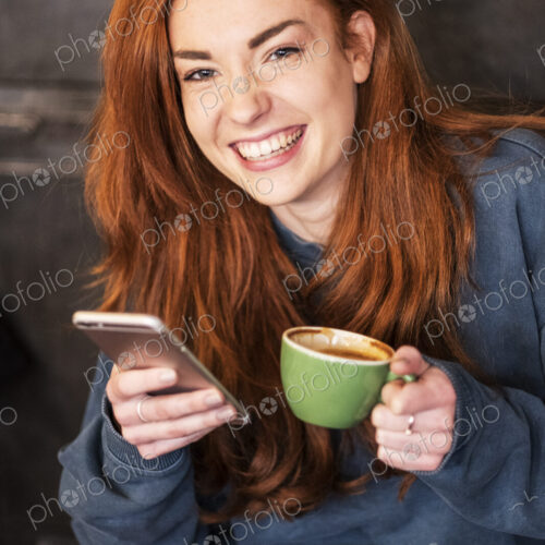 Smiling young woman holding mobile phone and coffee, working from home