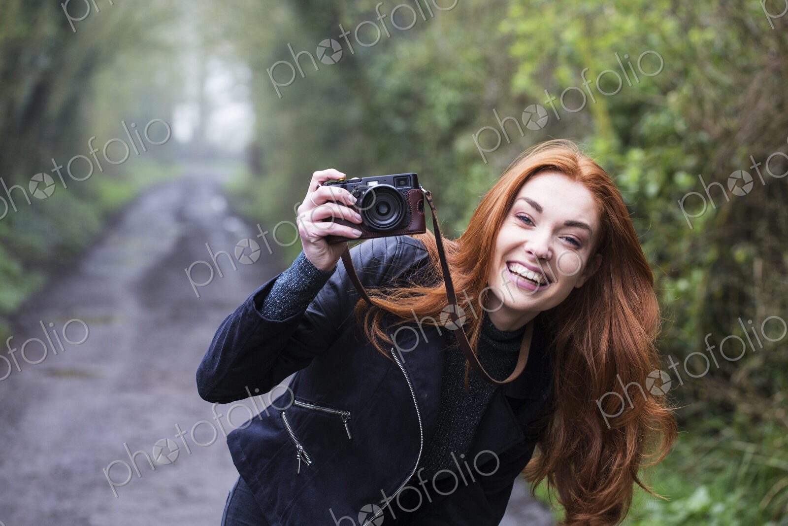 Smiling young woman outdoors taking pictures with vintage camera.