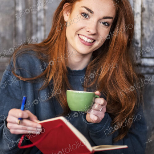Smiling young woman sitting at table with notebook and coffee, working Smiling young woman sitting at table with notebook and coffee, working