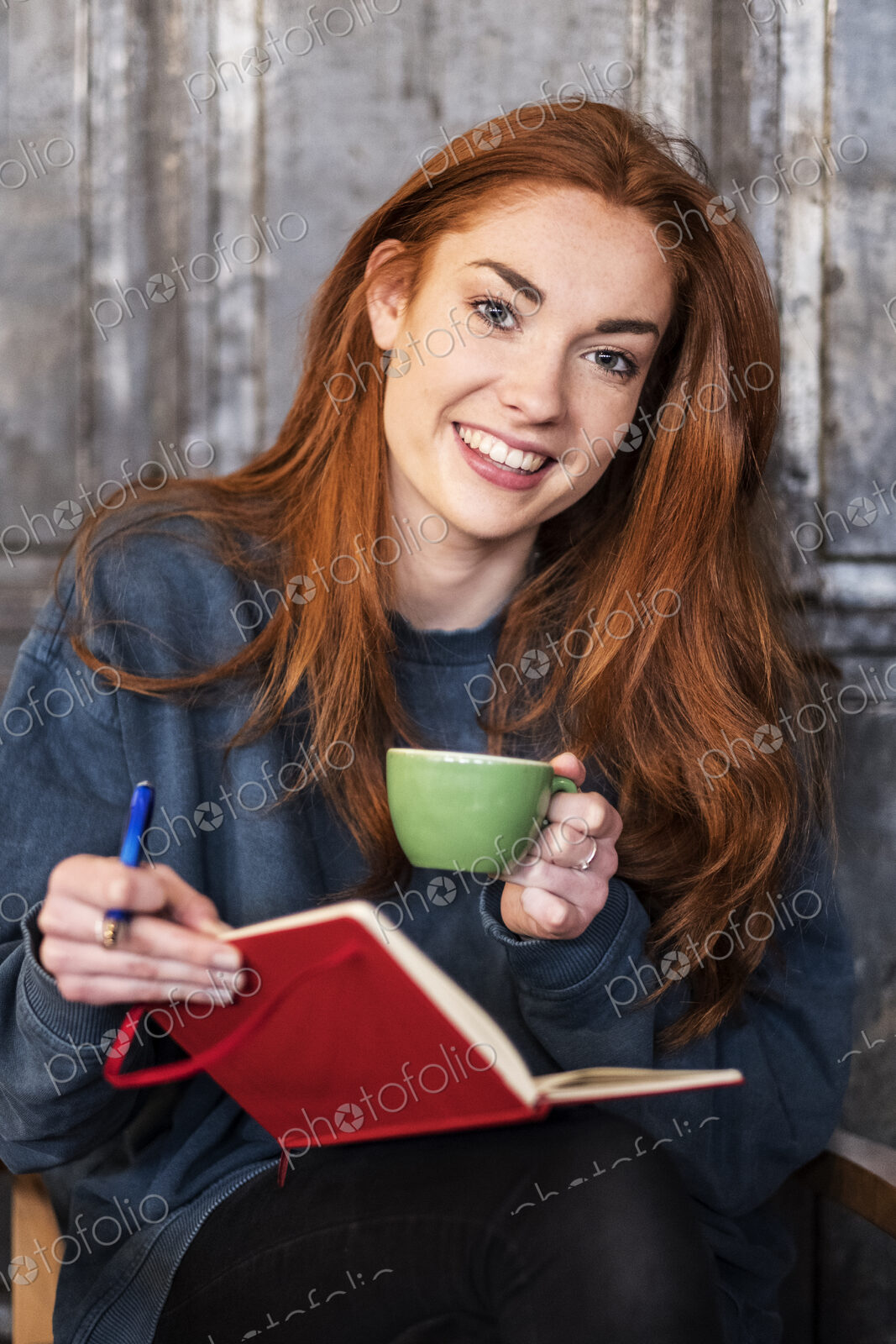Smiling young woman sitting at table with notebook and coffee, working