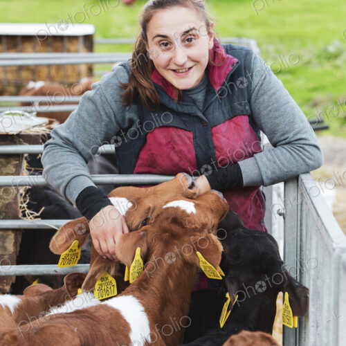 Smiling young woman standing next to metal pen with brown and black calves.