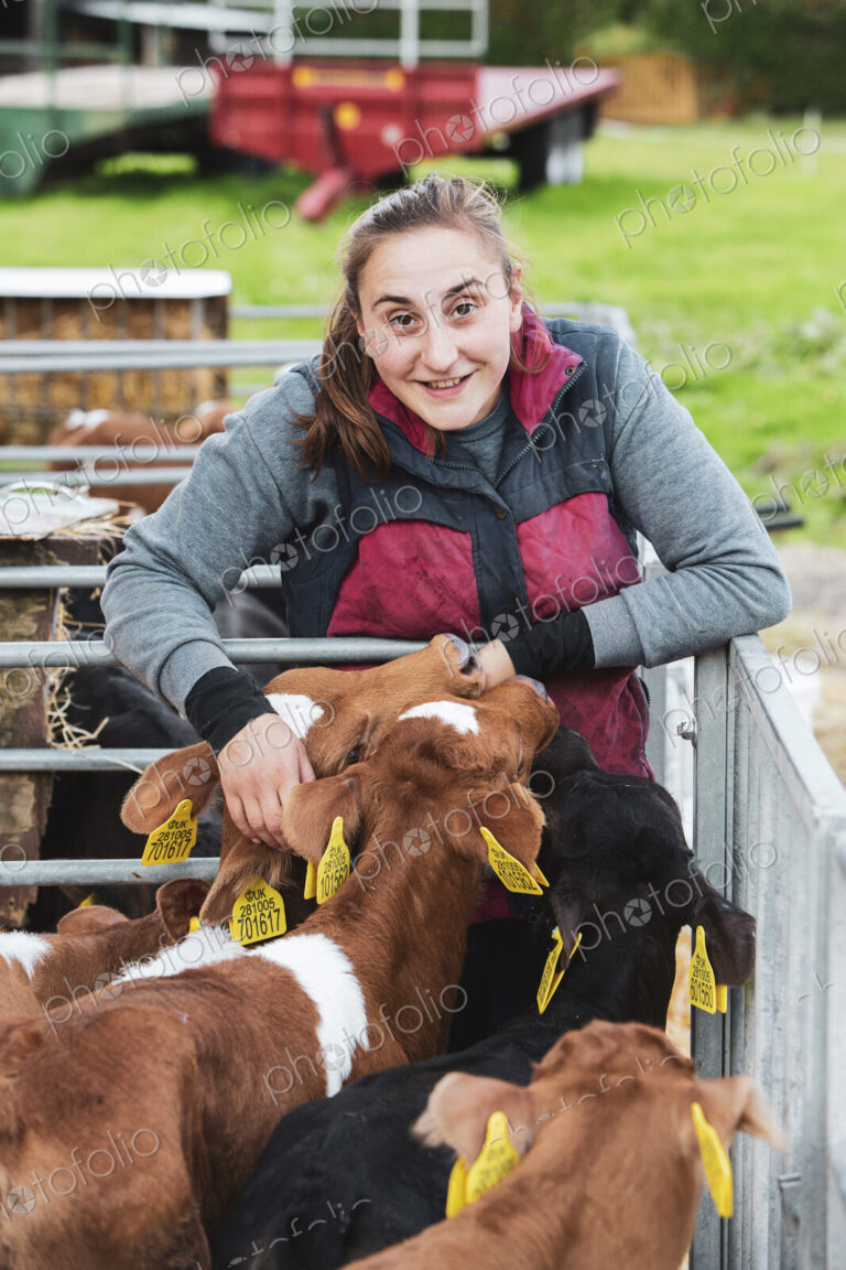 Smiling young woman standing next to metal pen with brown and black calves.