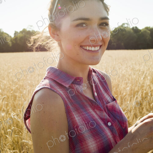 Smiling young woman wearing a checkered shirt standing in a cornfield. Smiling young woman wearing a checkered shirt standing in a cornfield.