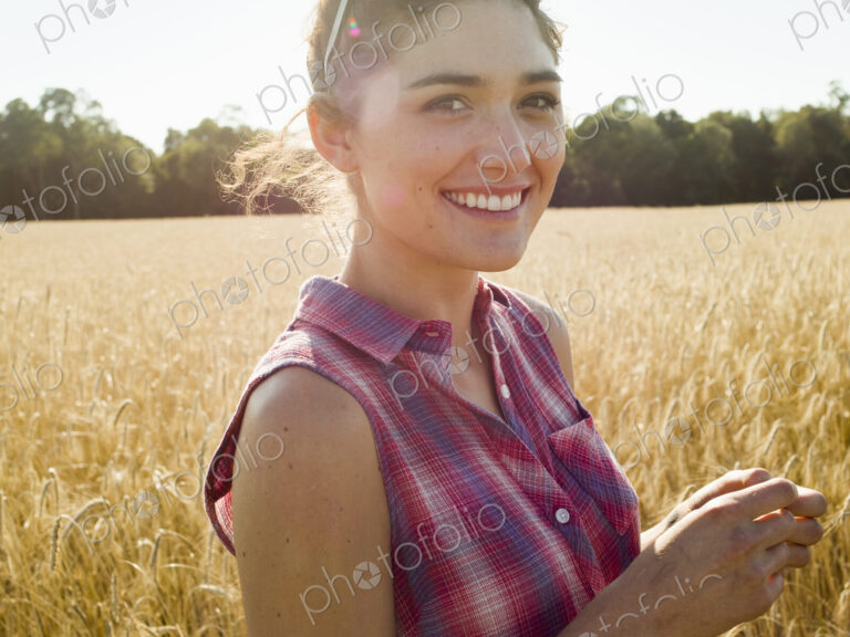 Smiling young woman wearing a checkered shirt standing in a cornfield.