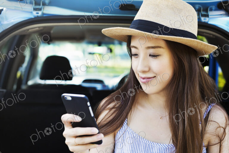 Smiling young woman with long brown hair, wearing Panama hat, using a mobile phone.