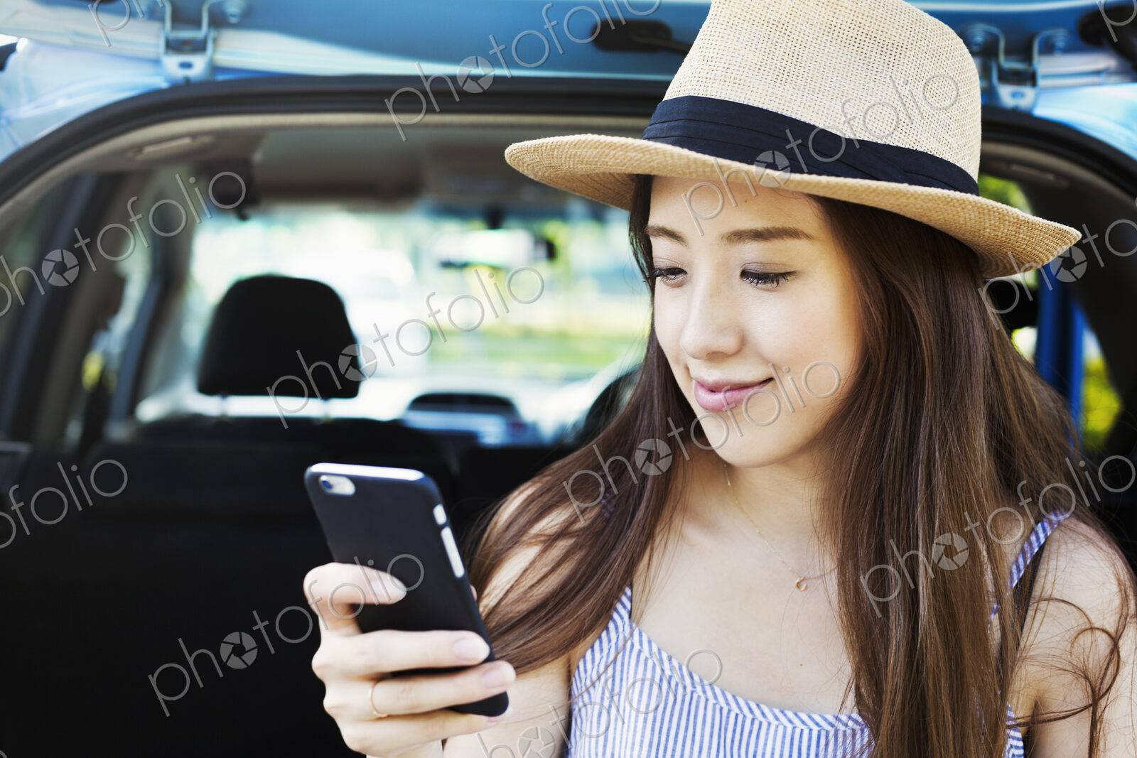 Smiling young woman with long brown hair, wearing Panama hat, using a mobile phone.