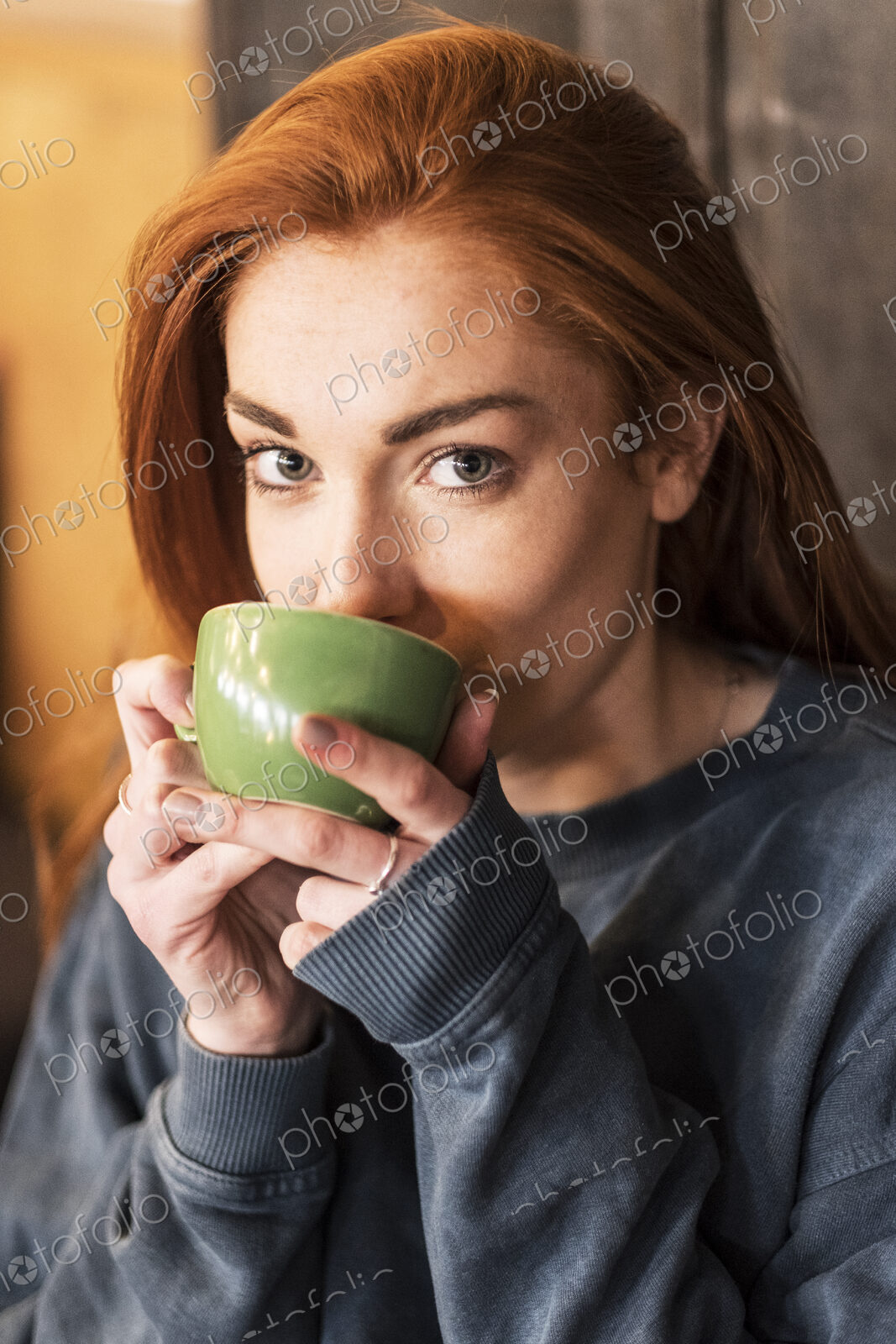 Smiling young woman with long red hair holding cup of coffee, looking at camera.