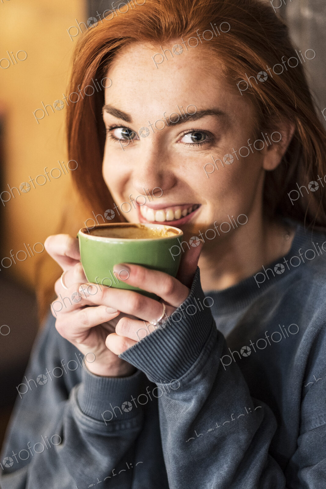 Smiling young woman with long red hair holding cup of coffee, looking at camera.