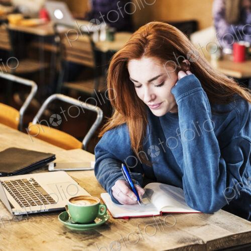 Smiling young woman with long red hair sitting at table, working on laptop computer. Smiling young woman with long red hair sitting at table, working on laptop computer.