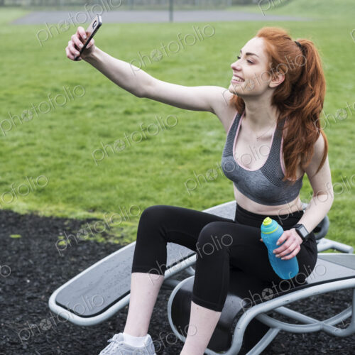 Smiling young woman with long red hair wearing sportswear, exercising outdoors. Smiling young woman with long red hair wearing sportswear, exercising outdoors.