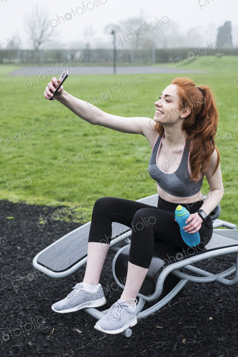 Smiling young woman with long red hair wearing sportswear, exercising outdoors.