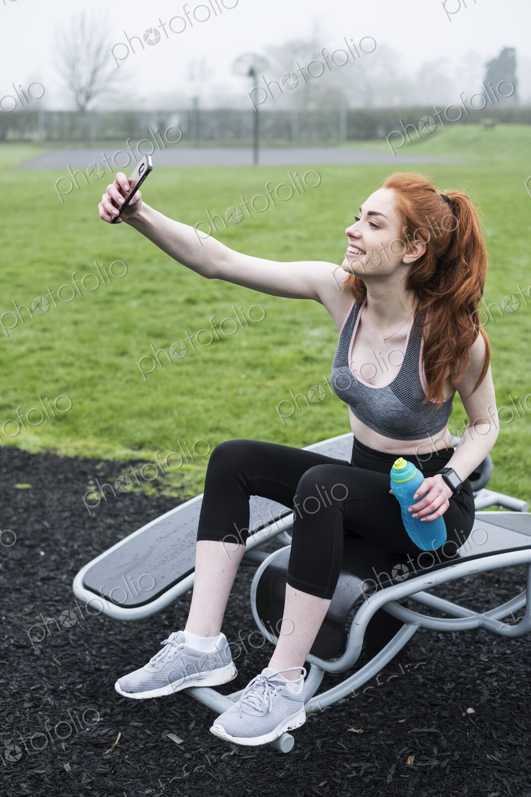 Smiling young woman with long red hair wearing sportswear, exercising outdoors.
