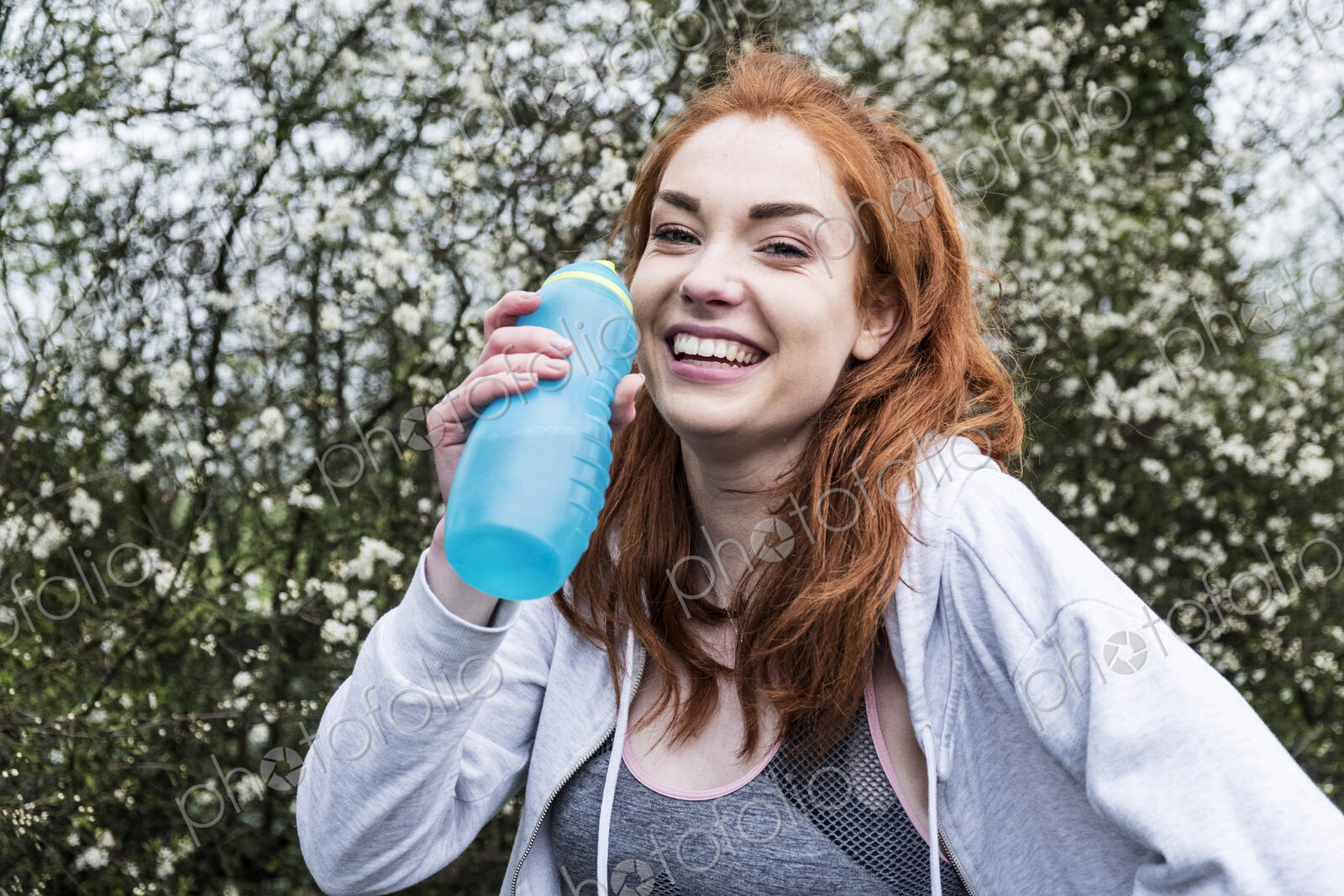 Smiling young woman with long red hair wearing sportswear, exercising outdoors,…