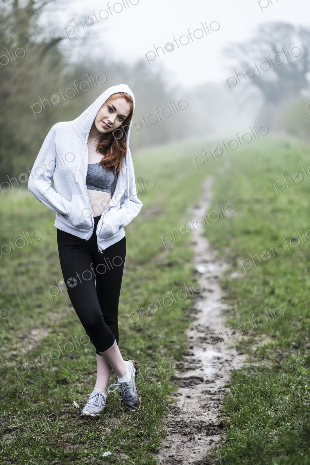 Smiling young woman with long red hair wearing sportswear, exercising outdoors,…