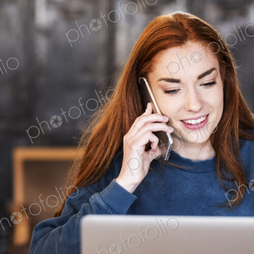 Smiling young woman working on laptop using mobile phone. Smiling young woman working on laptop using mobile phone.