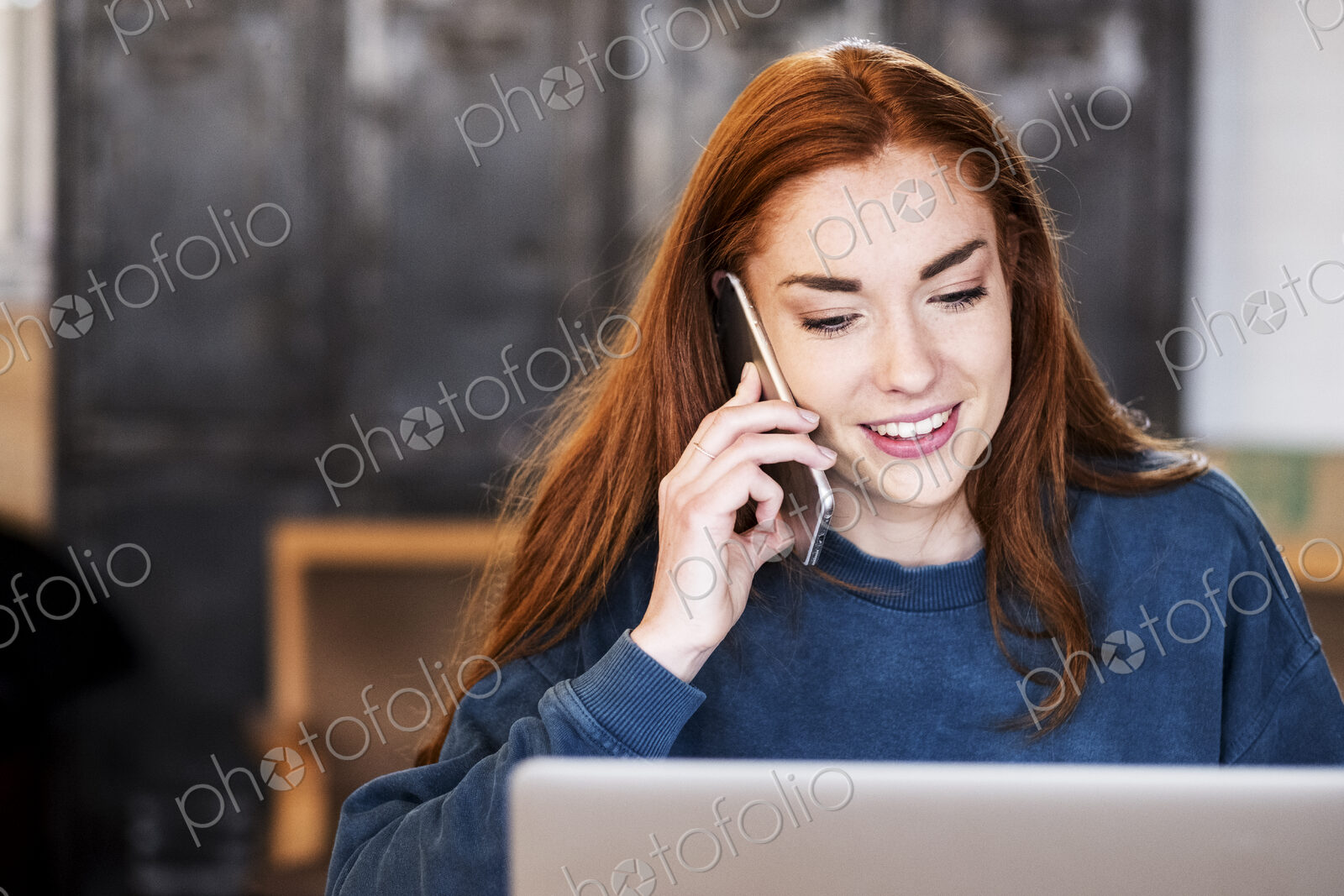 Smiling young woman working on laptop using mobile phone.