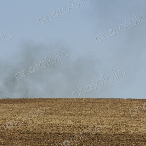 Smoke rising above a ridge, viewed across a ploughed field. Farmland near Pullman,…