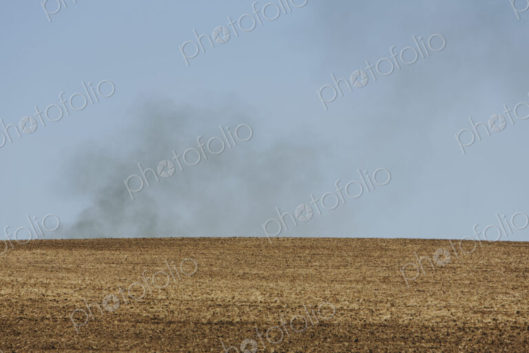 Smoke rising above a ridge, viewed across a ploughed field. Farmland near Pullman,…