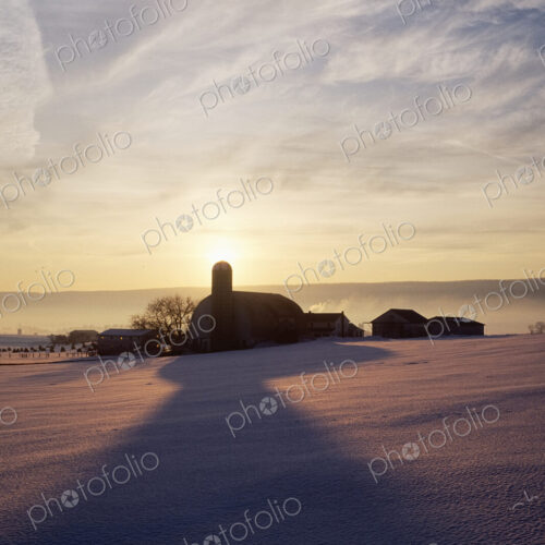 Snow Covered Field with Farm Silhouette at Sunset